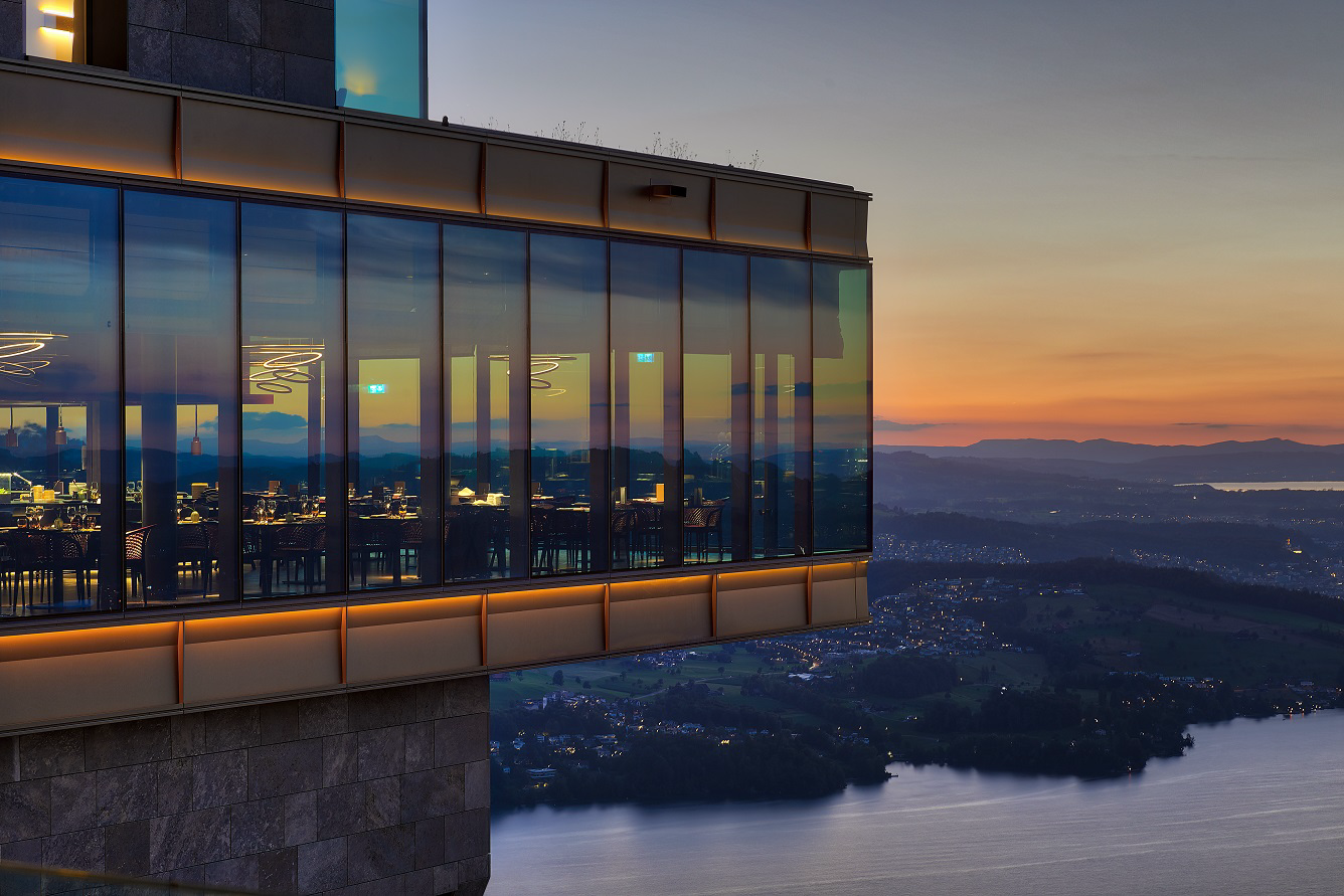 Cliffside restaurant with panoramic glass walls overlooking a lake at sunset