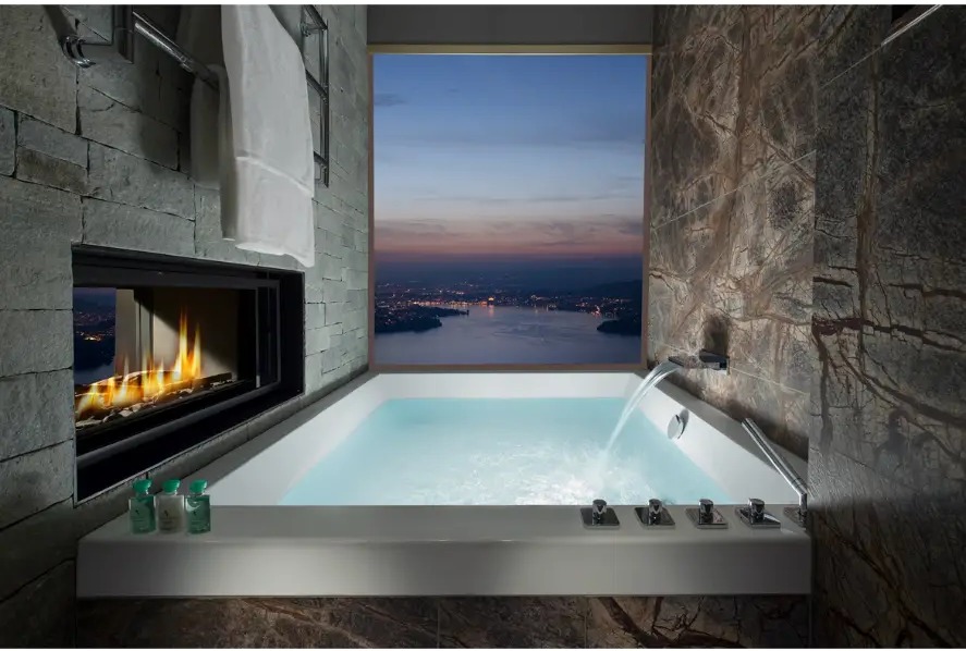 Luxury hotel bathroom with a soaking tub, fireplace and city view at dusk