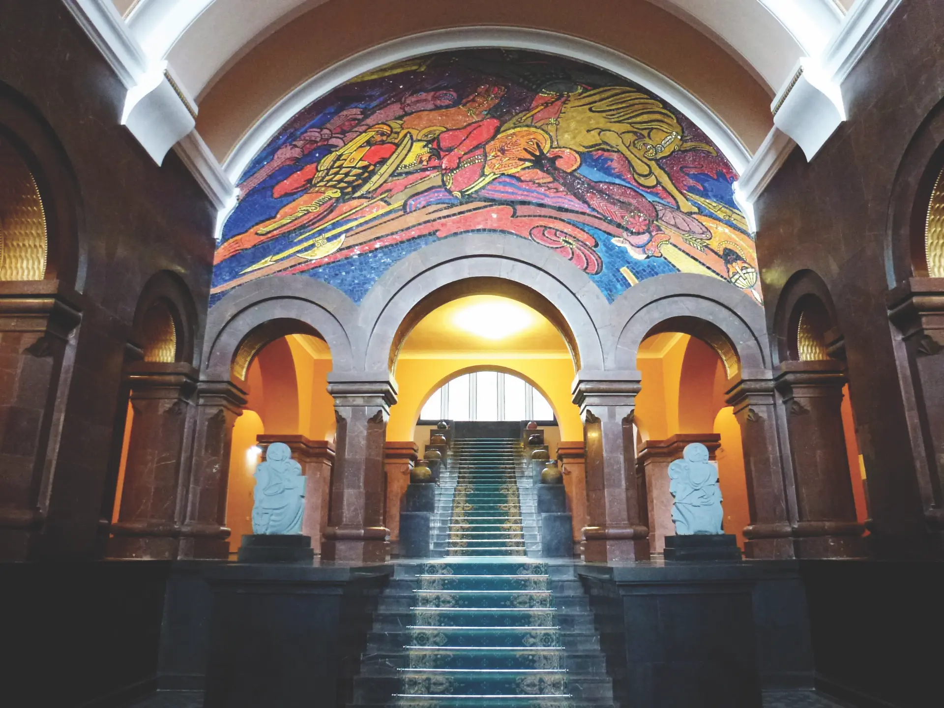 Grand vaulted lobby staircase beneath a vivid mosaic mural