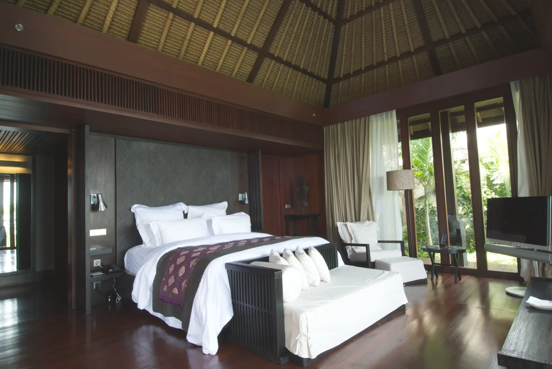 Thatched-roof villa bedroom opening onto tropical gardens