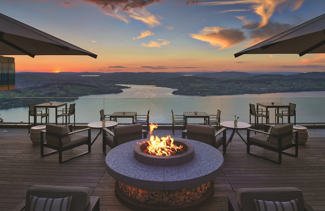 Outdoor fire pit lounge on a terrace overlooking a lake at sunset